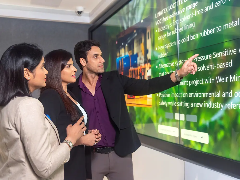 A customer experience tour guide showing two customers interactive content in the Infinity Room of the Technology Center Mumbai.