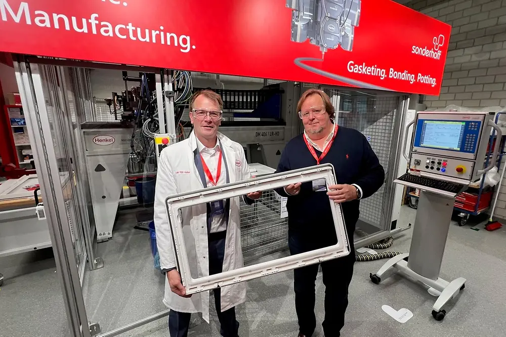 
Harald Dekkers, Dometic Product Area Manager for Windows, Blinds, Doors & Sanitary and Peter Fischer, Henkel Senior Manager Market & Customer Activation, present a Dometic window frame sealed with PU foam, standing in front of the Sonderhoff mixing and dosing system in Henkel's ICD laboratory (Düsseldorf).
